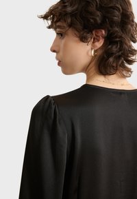 Blusa negra con tejido texturizado, mangas abullonadas y cuello redondo, con un acabado suave y una silueta elegante.