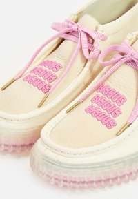 Baskets en cuir beige avec des lacets tissés rose et un branding. Elles présentent une semelle translucide teintée de rose et des accents en métal doré.