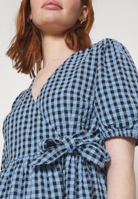 Klänning med C-halsringning i blå och svart rutig mönster, med korta puffärmar och ett knyt i midjan, samt en texturerad tygfinish.