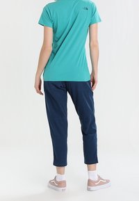 Turkusowa koszulka z krótkim rękawem, granatowe spodnie i jasnobrązowe trampki. Minimalistyczny design z logo na plecach koszulki.