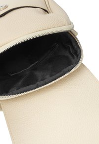 Zaino in pelle beige con superficie esterna texturizzata, apertura con zip e foderato internamente in tessuto nero. Include una tasca interna.