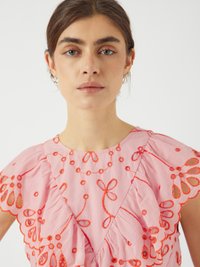 Abito rosa con maniche a volant e motivi floreali ricamati in rosso. Presenta intagli intricati e una scollatura a V.