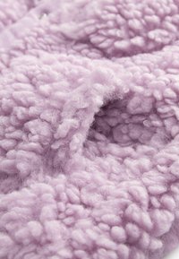 Ljuslila fleece-tyg med en texturerad, fluffig yta, som har en mjuk, oregelbunden hög och synliga sömnadsdetaljer.