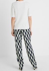 Valkoinen neulottu lyhythihainen pusero, jossa on tekstuuri kuvio, yhdistetty korkeavyötäröisiin housuihin, joissa on geometrinen laivastonsininen ja mintunvärinen timanttikuosi.