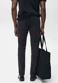 Jeans de mezclilla negros con corte ajustado y dos bolsillos traseros, combinados con un bolso tote negro y zapatos negros. El fondo es de color gris claro.