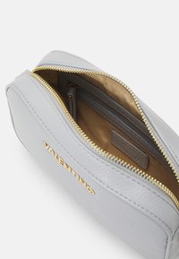 Pochette in pelle grigia chiara con una cerniera dorata, dotata di una sola tasca interna e una finitura testurizzata. Marchiata "Valentino" sul fronte.