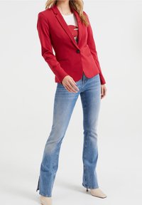 Röd skräddarsydd kavaj med långa ärmar och enkel knappstängning, bärs över en grafisk vit T-shirt och matchas med utsvängda blå jeans.