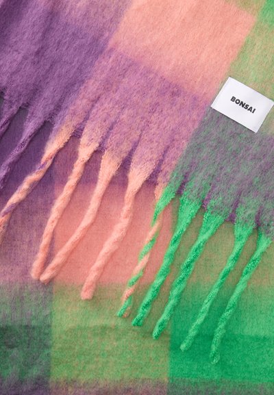 Cachecol de lã multicolorido com tons de roxo, rosa e verde. Bordas com franjas notáveis e um pequeno rótulo branco com "Bonsai."