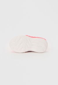 Vit texturerad sula på en rosa träningsskor sedd från botten mot en ren vit bakgrund.