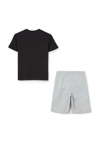 Camiseta negra de algodón con mangas cortas y cuello redondo, combinada con pantalones cortos de cintura elástica en gris claro, fabricados con un tejido suave.