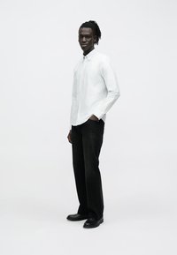 Camisa blanca a rayas con botones combinada con jeans negros de corte relajado y zapatos negros. Textura suave con colores contrastantes y diseño sencillo.
