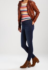 Brun läderbikerjacka, flerfärgad randig långärmad tröja, mörk denim skinny jeans, bruna ankelboots med spänne.