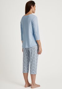  Lichtblauw langarmshirt met een ronde hals, gecombineerd met gestreepte capri-broek met een bloemenpatroon in donkerblauw en wit.