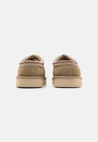 Bruine suède instapschoenen met een gestructureerde kraag en een lichtbeige rubberen zool, met contrasterende stiksels rondom de rand.