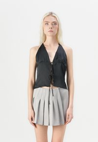 Crna halter majica s detaljem vezanja sprijeda, izrađena od glatke tkanine. Uparena s siva mini suknja s nabiranim detaljima, koja ima strukturirane nabore.