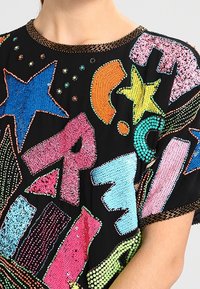 Svart topp med färgglada, glittrande bokstäver och stjärnor i olika former. Dekorerad med texturerade paljetter och ett mönstrat halsband.