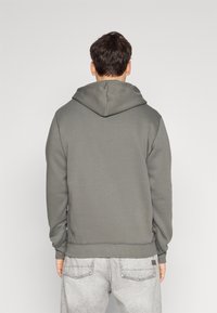 Felpa con cappuccio grigia realizzata in tessuto morbido, con polsini e orlo a costine. Presenta un design classico con una vestibilità rilassata e senza marchi visibili.