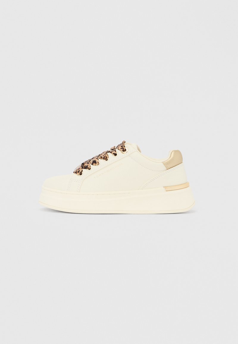 Sneaker bele barve s debelejšim podplatom, vezalkami z leopardjim vzorcem, zlato petno zanko in subtilnim logotipom Tommy Hilfiger na strani, prikazan od strani.