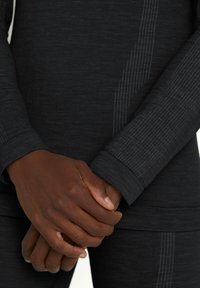 Czarna bluzka z długim rękawem wykonana z teksturowanej tkaniny z subtelnymi poziomymi i pionowymi paskami. Mankiety są ściągane i dopasowane, podkreślając przylegający krój.