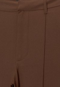 Rjave hlače iz gladkega blaga, z oprijetim krojem, diskretnim stranskim žepom in ravnim sprednjim delom z minimalnimi šivi.