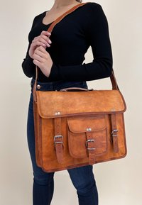 Brun læder budetasker med en frontklap, to spændebånd og en frontlomme. Tasken har en glat overflade og sølvfarvede hardware-akcenter.