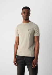 Gai beigains īsām piedurknēm T-krekls, kas izgatavots no kokvilnas ar noapaļotu kakla izgriezumu. Satur nelielu izšuvumu ar kafijas krūzi un vīna glāzi.