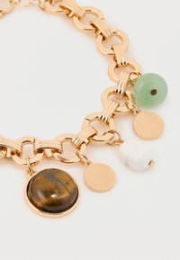 Guldtonet metalarmbånd med sammenkædning, tre dekorative accenter: en rund tigerøje, en grøn perle og en hvid sten.