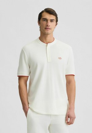 Korte mouw, crèmekleurige polo met een rode accent bij de kraag en mouwen, voorzien van een knoopsluiting bij de hals en een klein logo op de borst.