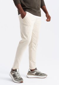 Crème joggings met zijzakken en een slim fit, gecombineerd met grijze en witte sportschoenen met textuuraccenten.