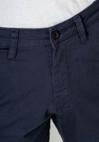 Navy blue cotton trousers feature a button closure, side pockets, and a smooth texture with reinforced stitching along the seams.