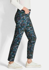 Donkerblauwe broek met een bladertpatroon in groene en bruine tinten, met een slim fit en zijzakken, gecombineerd met witte sneakers.