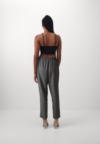 Top court noir et pantalon de survêtement satiné gris. Dispose d'une taille élastique et de jambes droites. Des chaussures à talons transparents complètent le look.