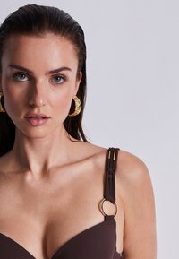 Haut de bikini marron avec armatures, fabriqué en tissu texturé, doté de bretelles tressées et d'accents en métal doré en forme de cercle.