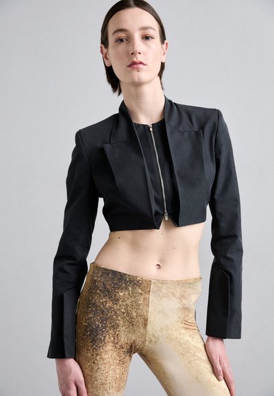 Black cropped jacket with a front zipper and tailored sleeves, paired with gold and brown patterned leggings featuring a textured finish.