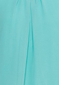 Ljus turkos tyg med en vertikal mittveck som skapar subtila vikningar och textur.