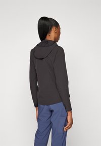 Giacca nera con cappuccio, con una finitura testurizzata, caratterizzata da maniche lunghe e una vestibilità rilassata, abbinata a pantaloni cargo blu con tasche laterali.