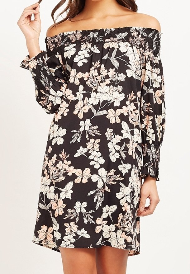 Femme portant une robe noire épaules dénudées avec des manches longues et un motif floral blanc et beige.