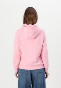 Sweatshirt rose clair avec capuche, poignets et ourlet côtelés. Texture douce et coupe décontractée, associé à un jean large bleu.