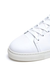 Sneaker bianca in pelle con punta arrotondata, suola piatta e suola in gomma testurizzata; presenta dettagli grigi e un classico design con lacci.