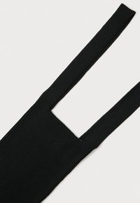 Tecido de malha canelada preto com duas alças largas, formando um recorte retangular entre elas, sobre um fundo branco.