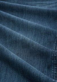 Mørkeblå denimstoff med en myk tekstur, preget av subtile fargevariasjoner og et klassisk vevd mønster. Glatt, brettet i lag.