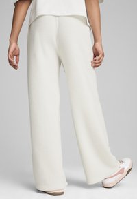 Pantalones de felpa anchos en color blanco roto con una textura suave, que presentan un acabado liso y un ligero acampanado en el dobladillo, combinados con zapatillas ligeras.