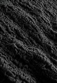 Tissu noir texturé avec un motif froissé, présentant des sections surélevées irrégulières et une surface douce, légèrement duveteuse.