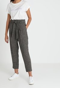 T-shirt blanche avec le texte "INFLUENCER", associée à un pantalon taille haute grisé à motifs et des baskets blanches. Le pantalon est doté d'une ceinture nouée.