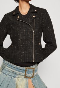 Czarna, krótka kurtka wykonana z fakturowanej tkaniny z złotymi nitkami, z zapięciem na zamek błyskawiczny, zatrzaskami i wyciętym kołnierzem. W komplecie ze spódnicą dżinsową.
