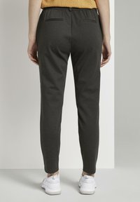 Grijze elastische broek met een taps toelopend ontwerp, voorzien van twee achterzakken. G gedragen met witte sportschoenen.