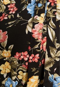 Schwarzer Stoff mit floralem Druck, der pinke, gelbe und blaue Blumen sowie grüne Blätter zeigt. Detaillierte Stiche und ein plissiertes Design sind zu sehen.