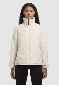 Chaqueta acolchada y puf, de color crema, con un alto cuello, que cuenta con un cierre frontal completo y bolsillos laterales con cremallera. Textura suave con patrón de diamantes.