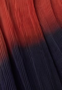 Geplooide stof met een verloop van diep rood aan de bovenkant naar donkerblauw aan de onderkant, die een fijne textuur en beweging laat zien.