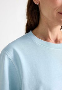 Lyseblå bomulds t-shirt med en klassisk rund halsudskæring, blød tekstur og synlige syninger langs halsudskæringen og skuldrene.